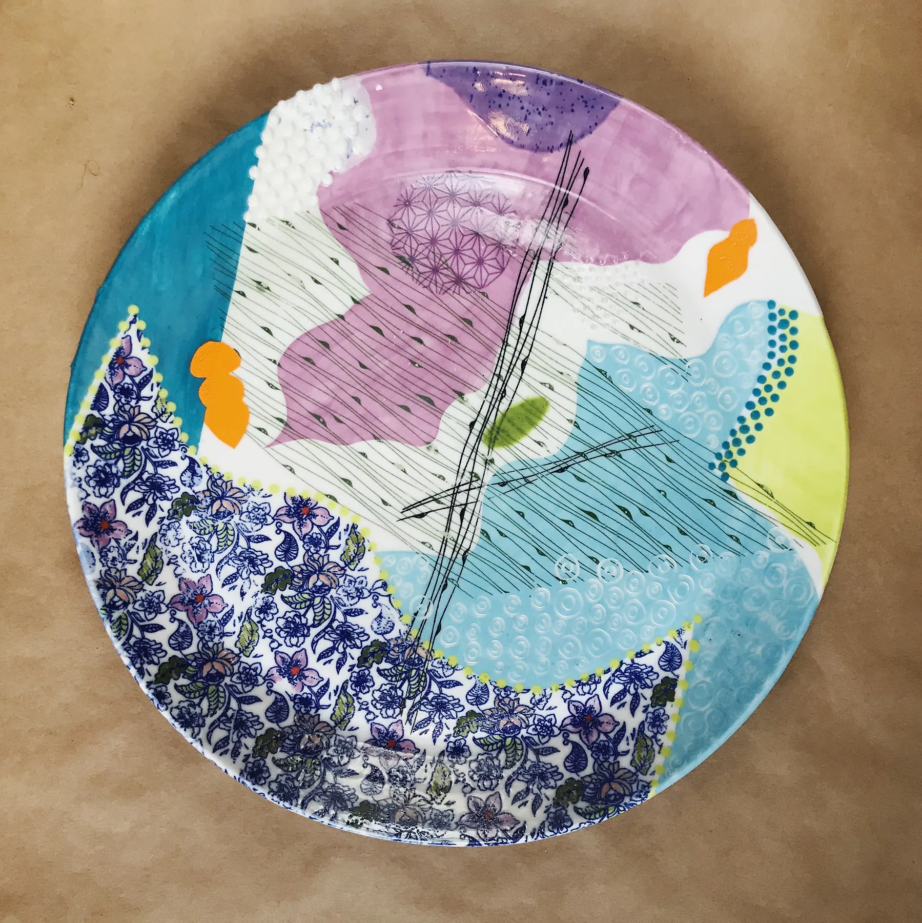 A large round porcelain platter layering a cobalt floral field, magenta and turquoise color blocks, chartreuse dots, orange marks, carved hatching and raised white beading.