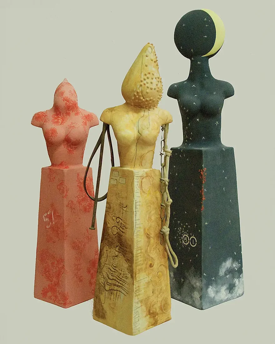 Three tall totemic ceramic figures in coral, ochre and deep teal.