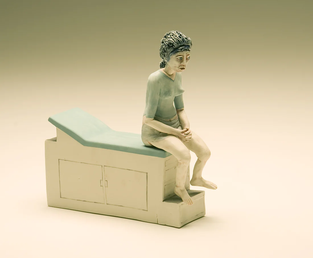 A small ceramic figure seated on an examination table.