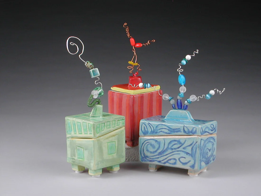 Three small footed ceramic boxes topped with looping wire.