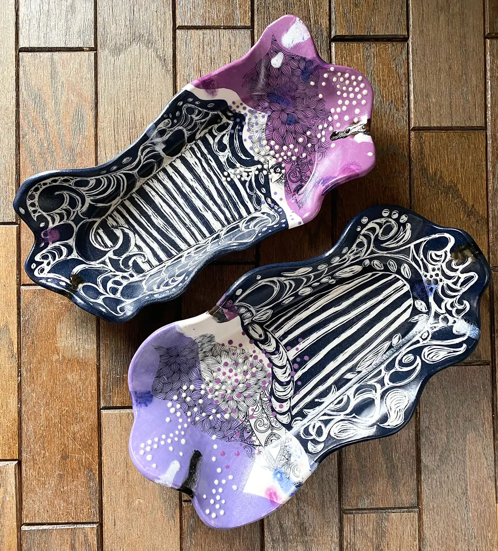 A pair of navy and violet sgraffito trays on dark wood.