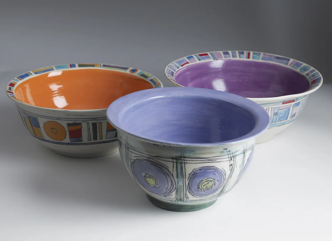 Three ceramic bowls glazed orange, lavender and blue inside.